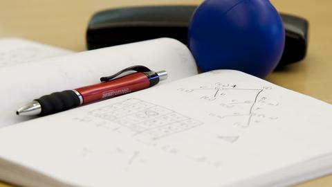 Notebook open to a page with diagrams and tables, with a pen, squeeze ball, and glasses case.