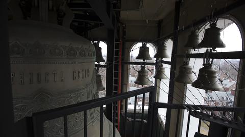 View from inside a bell tower showing a large central bell and smaller bells silhouetted against arched windows.