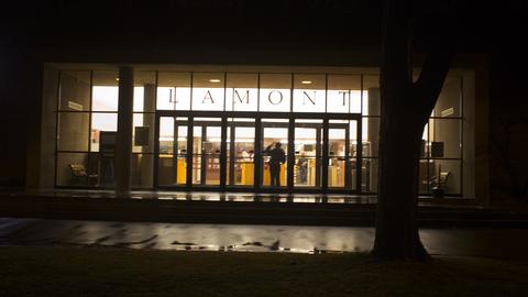 Exterior view of entrance to Lamont Library at night.