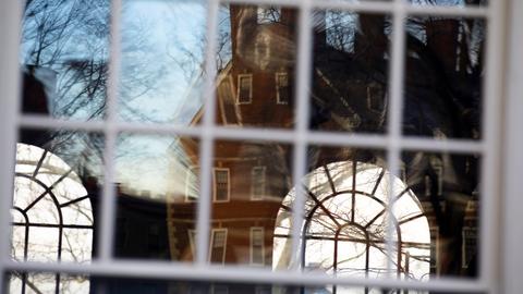 Window reflecting the sky, branches, and a building, with a view through to arched windows.