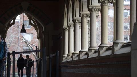Two people walking through an archway with columned windows.