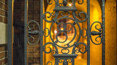 Lighted arched tunnel through the bars of a closed wrought iron gate.