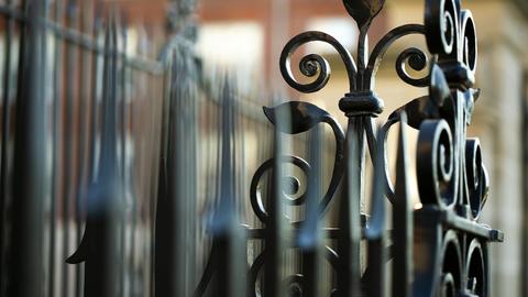 Close-up of ornate wrought iron gate with blurred buildings in the background.