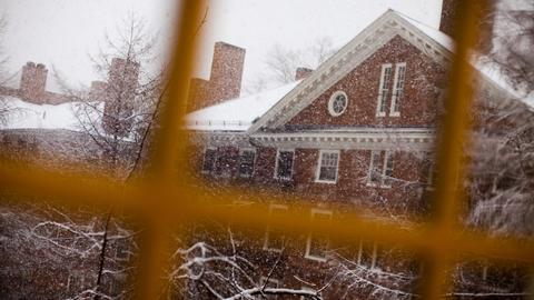 Snowy scene of a brick building with windows and chimneys, viewed through window panes.