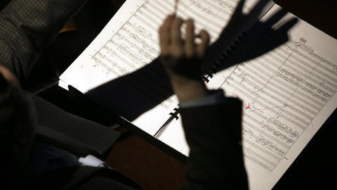 Conductor's hands casting a shadow on a musical notation sheet